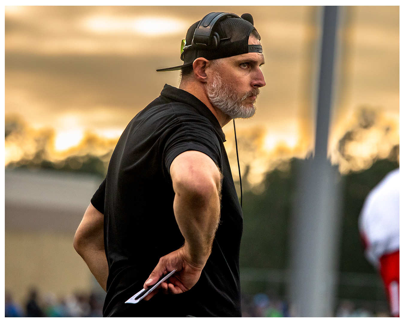 Coach Nate on the sideline with headset during a game at sunset