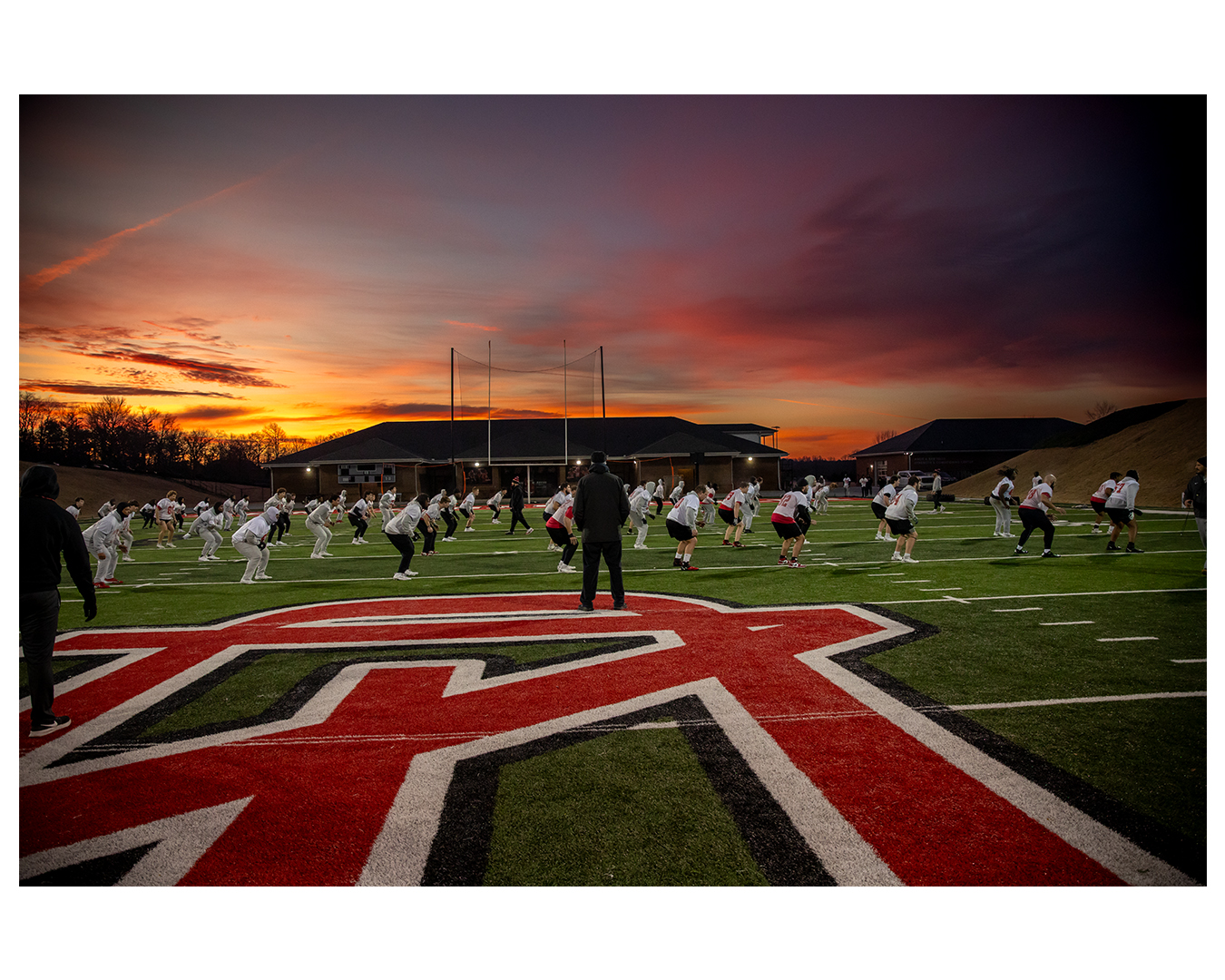 Coach Nate standing on the football field at sunset watching practice
